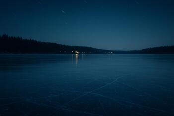 Ice shelter lit from inside on a frozen lake at deep night with stars above