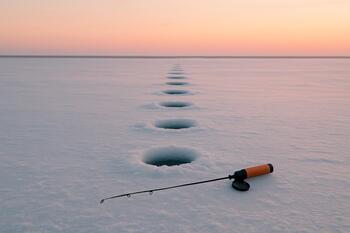 Row of drilled ice holes at dawn with a rod resting on the ice