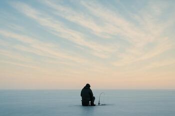 Morning ice sky with pale clouds above a single angler