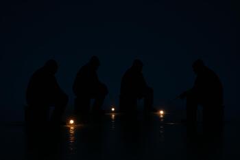Night silhouettes of anglers on ice with small lights glowing