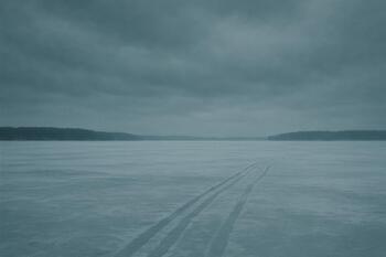 Quiet midwinter lake with overcast sky and a single angler near a hole